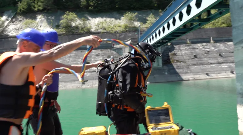 Echipa ajustează furtunul ombilical al scafandrului complet echipat, pe ponton, lângă lacul de acumulare.
